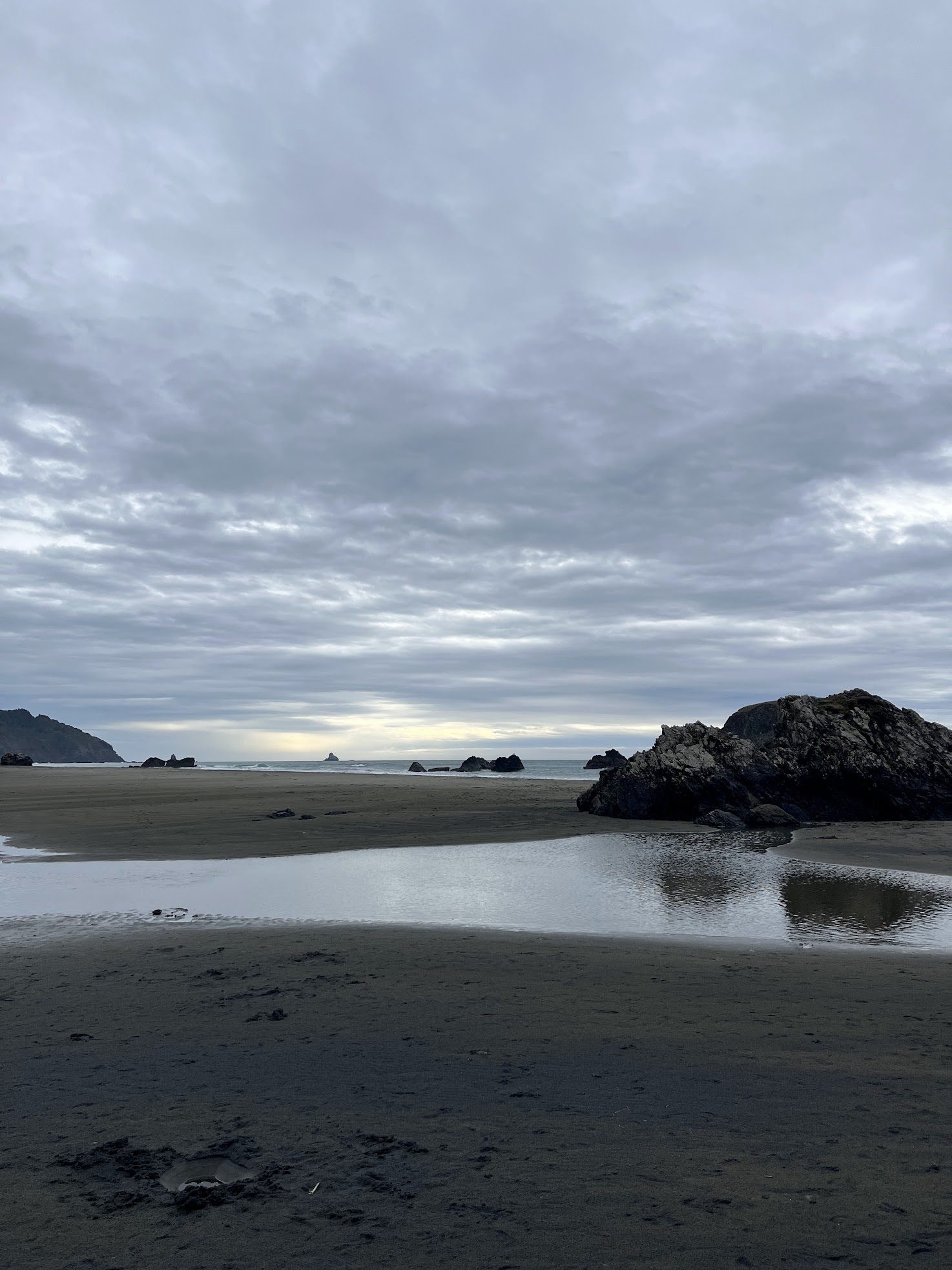 Overcast afternoon at Whaleshead Beach, rocks and creek lagoon under a soft grey sky.