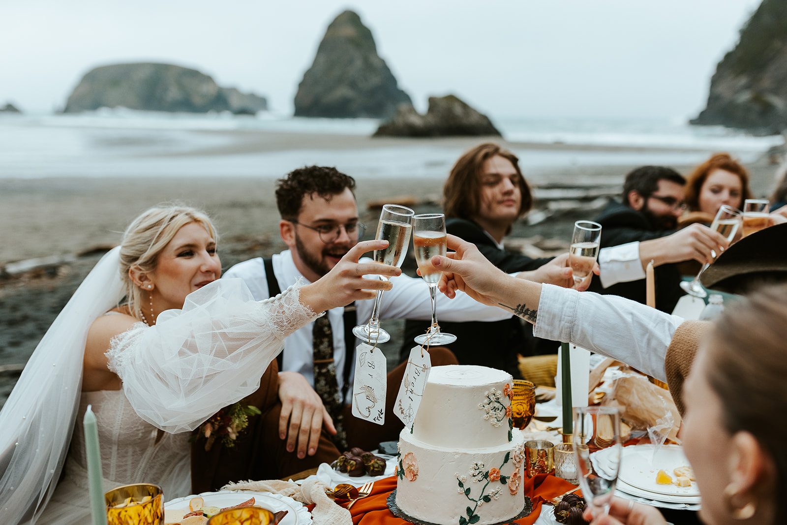 Wedding party raising champagne at a beach elopement picnic on the Oregon coast.