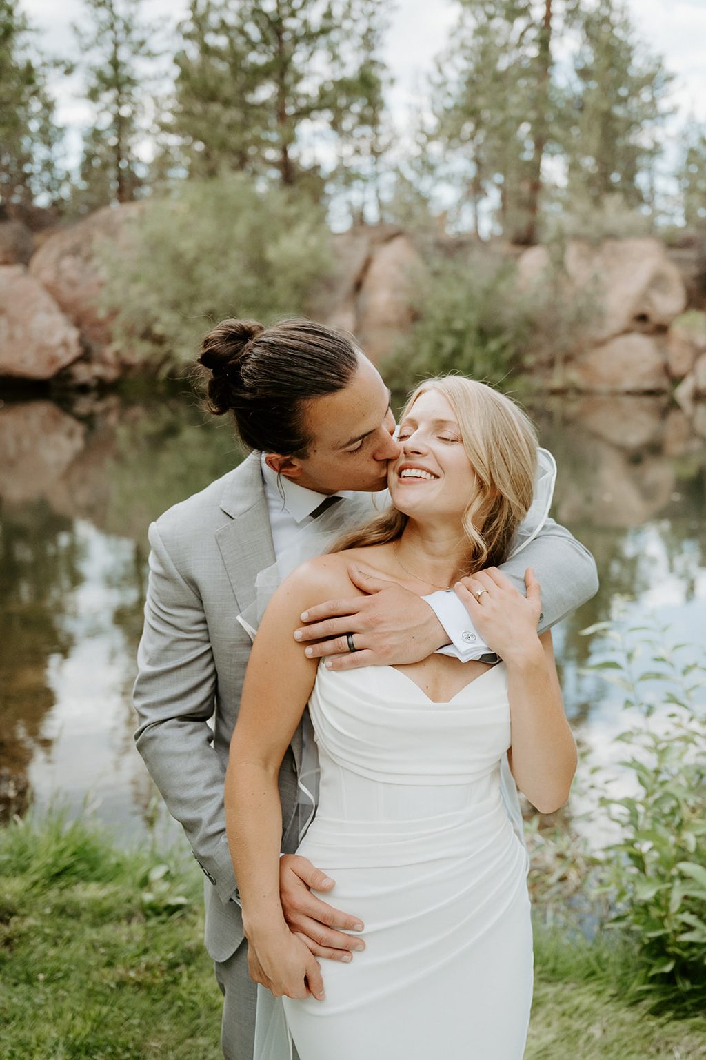 Couple by the pond at Rock Springs Ranch, dress train across the grass.
