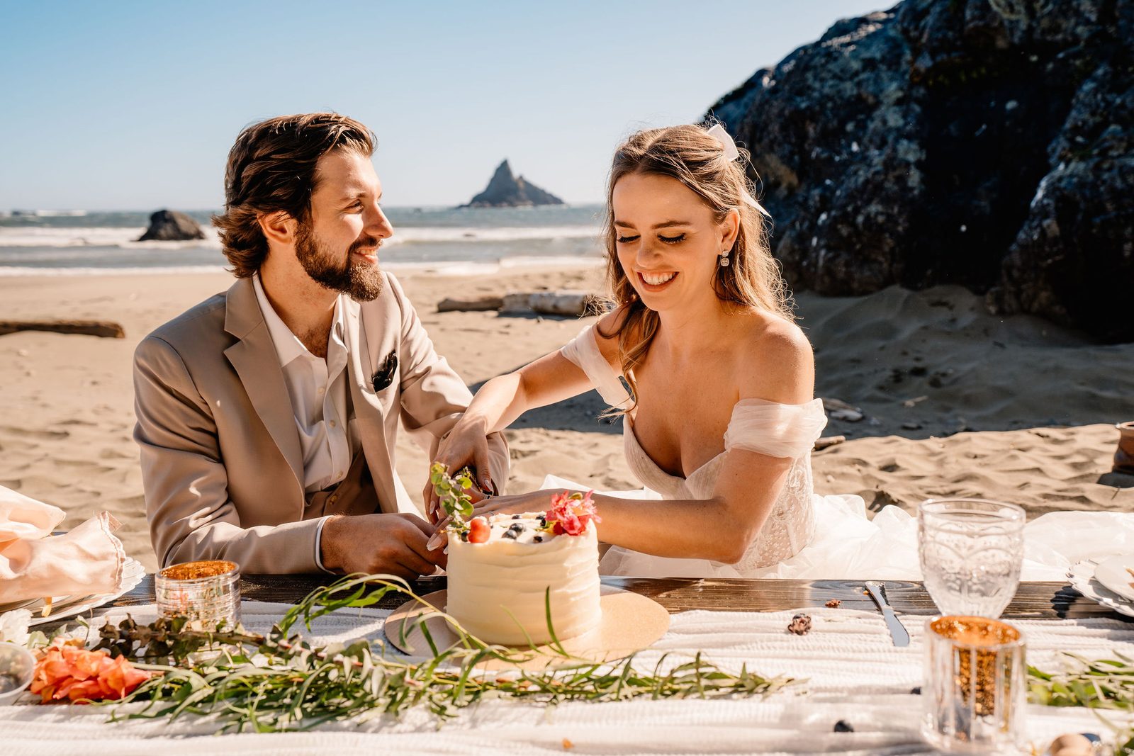 Couple cutting cake at a sunny beach elopement picnic.