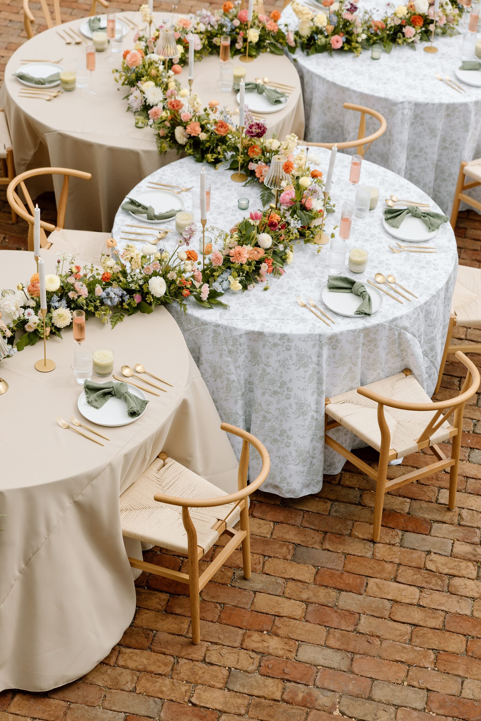 Round reception tables wrapped in floral garlands on a brick patio.