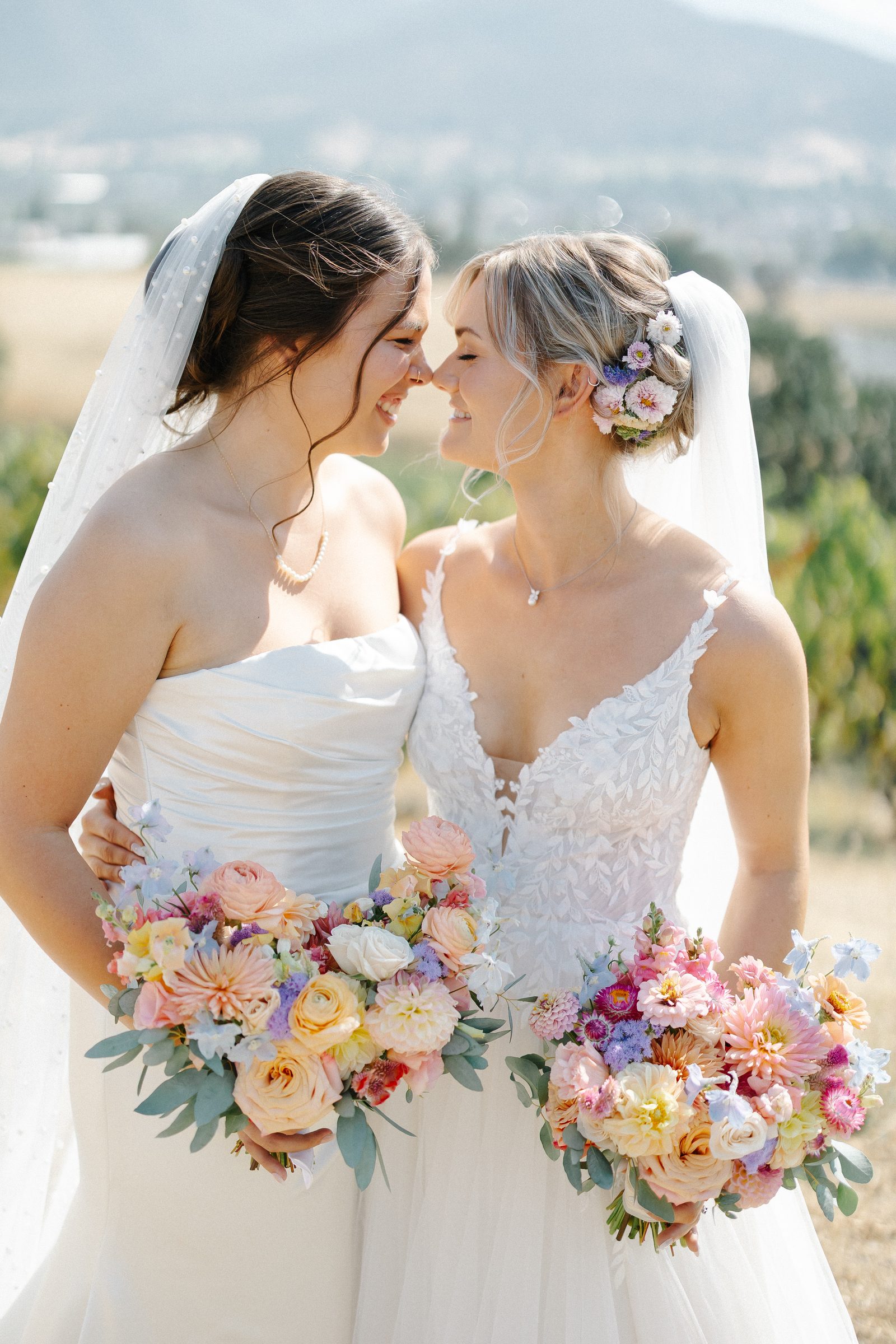 Two brides with pastel bouquets in a vineyard.