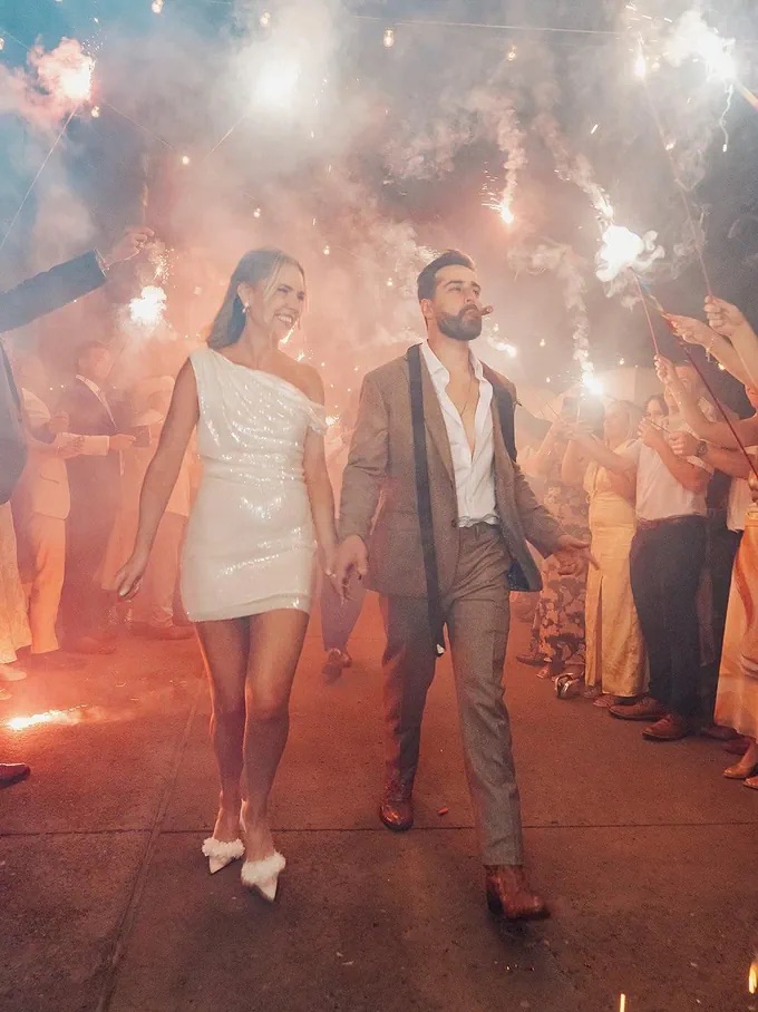 Newlyweds walking hand in hand through a sparkler send-off at night.